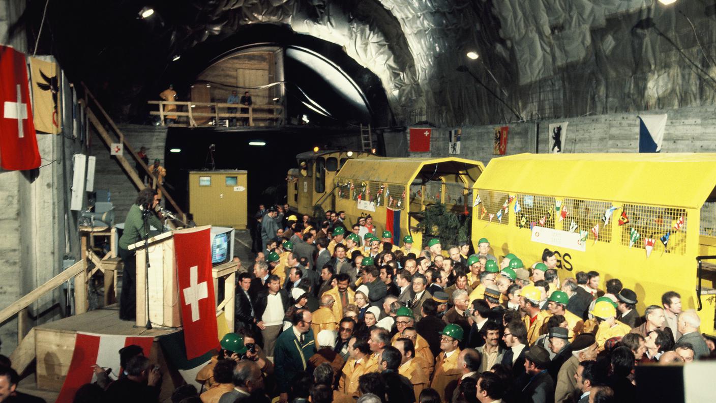 Pozzo di ventilazione di Motto di Dentro (versante sud), le/i presenti attendono la diretta: lo schermo accanto al pulpito (dal quale si potranno seguire i collegamenti con Hospental e con i minatori in servizio) mostra ancora il monoscopio.