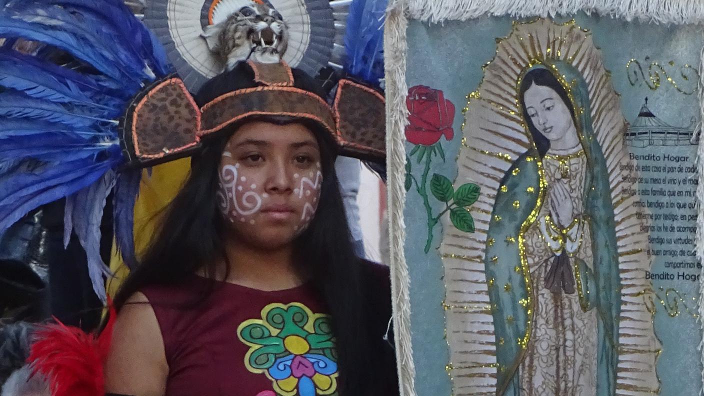 Una giovane danzatrice porta lo stendardo della 'Virgen de Guadalupe' durante una delle processioni della celebrazione, tra le più antiche e partecipate del Messico centrale. La festa, nata dall’incontro tra riti preispanici e pratiche cristiane dopo il 1531, si svolge attorno alla chiesa della Santa Cruz, luogo simbolico della mediazione tra tradizioni indigene e nuova religiosità coloniale.