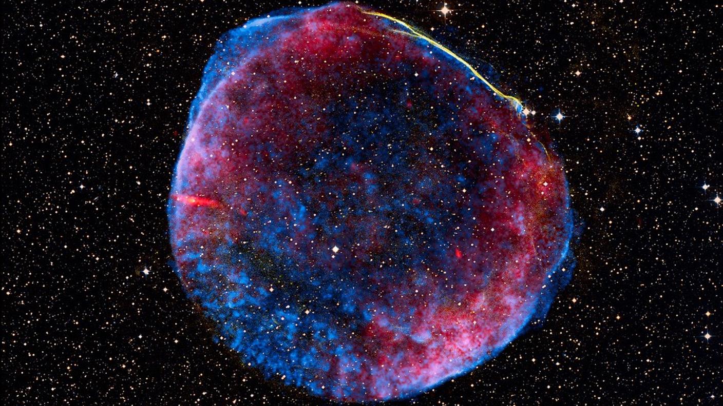 Immagine composita del remanente di SN 1006, a circa 7.000 anni luce dalla Terra, ripresa da Chandra: in rosso e verde il gas riscaldato a milioni di gradi, in blu elettroni accelerati a energie elevatissime. L’esplosione, avvenuta nel 1006, segnò la morte di una nana bianca che, superato il limite di stabilità, generò onde d’urto capaci di riscaldare il gas e accelerare particelle nello spazio.
