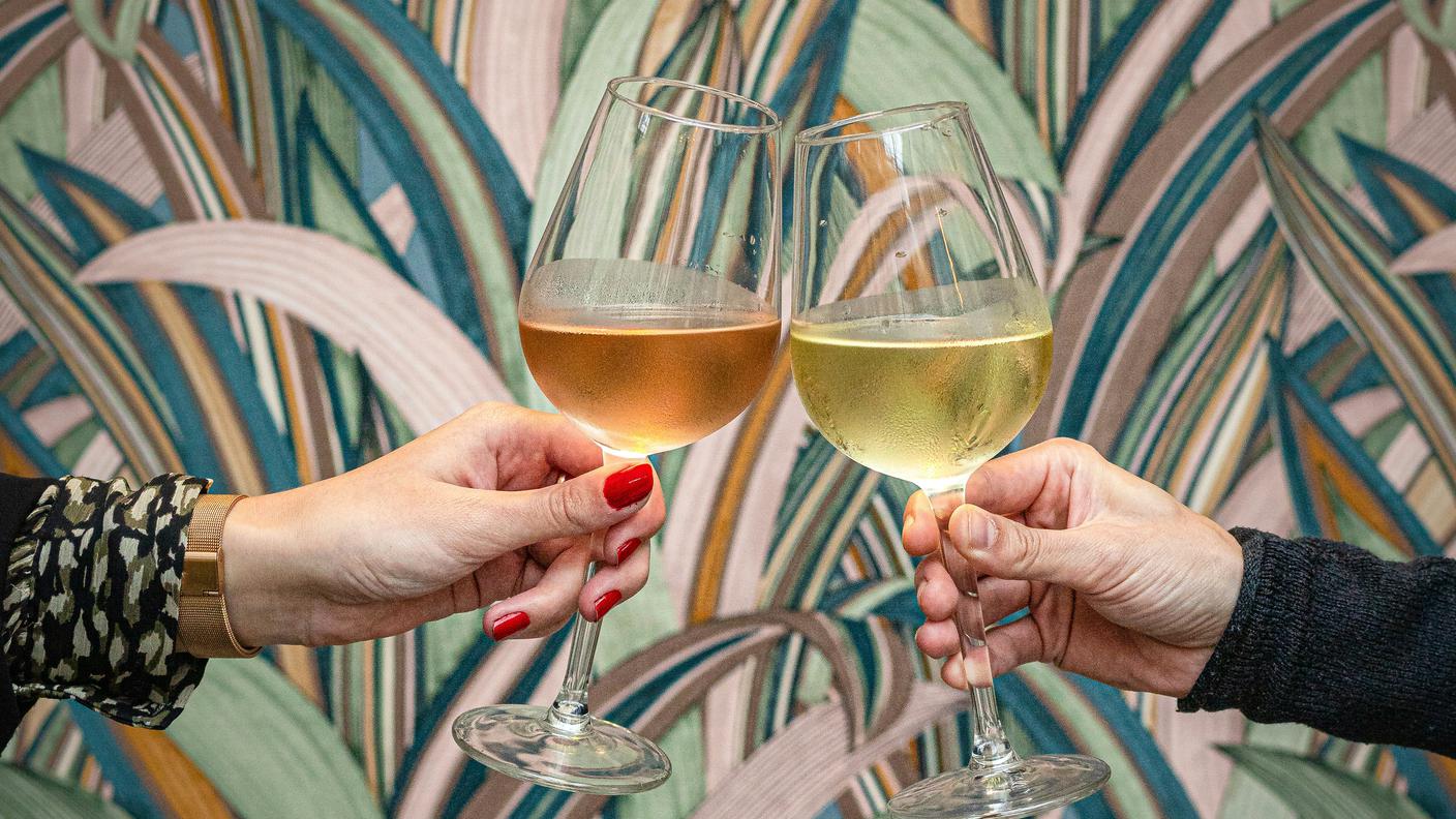 due calici di vino si incotrano per un brindisi su uno sfondo di carta da parati tropicale