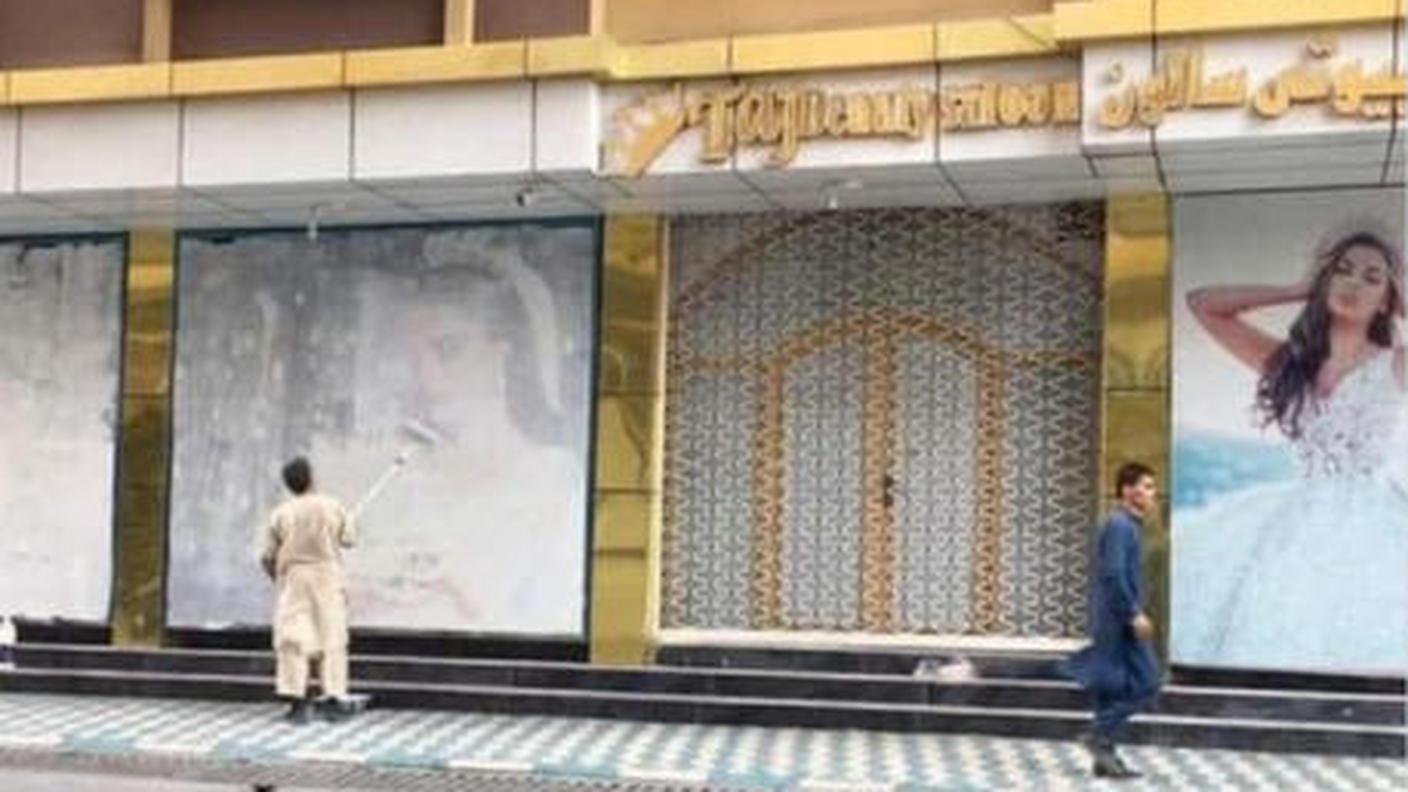 Un uomo che ricopre con della vernice alcuni poster che ritraggono donne su un muro a Kabul