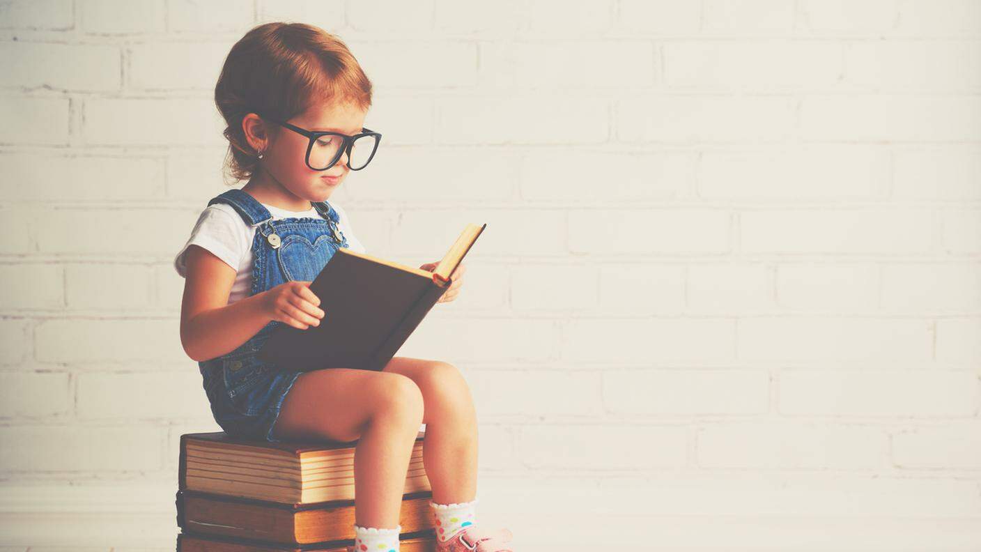 Bambino piccola bambina con gli occhiali di lettura di un libro