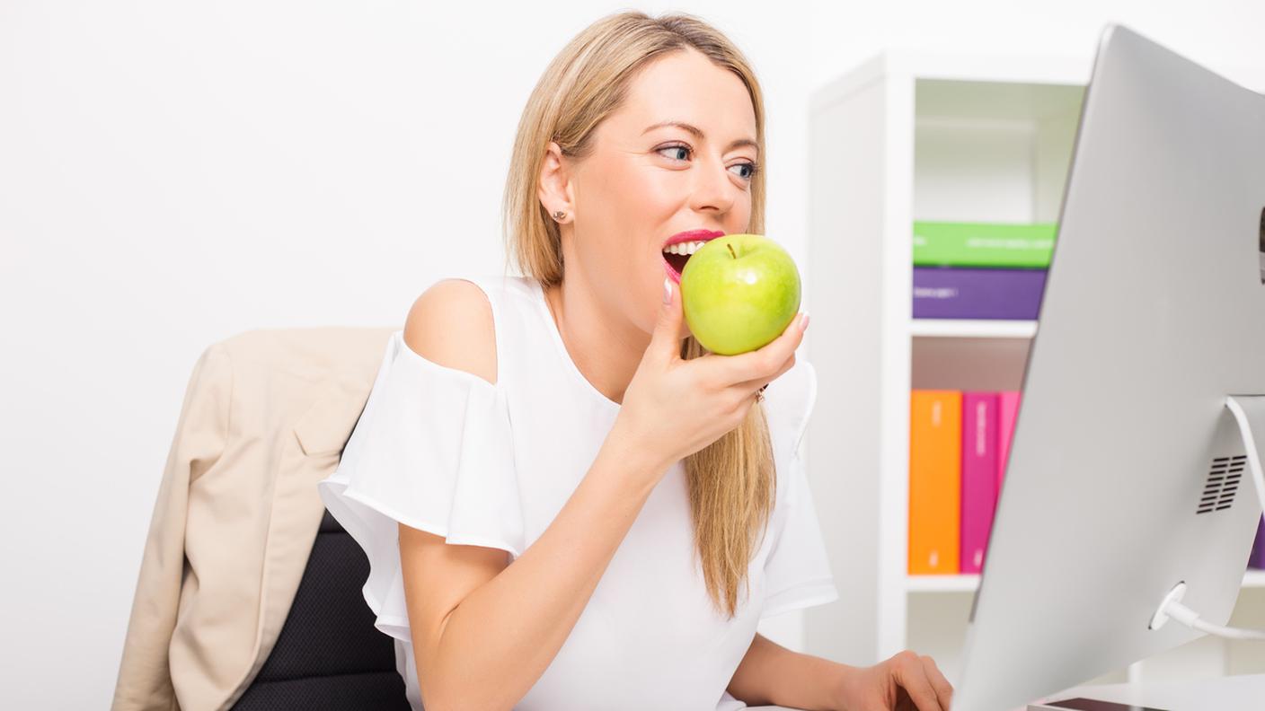Donna mangia frutta, lavorando su computer in ufficio