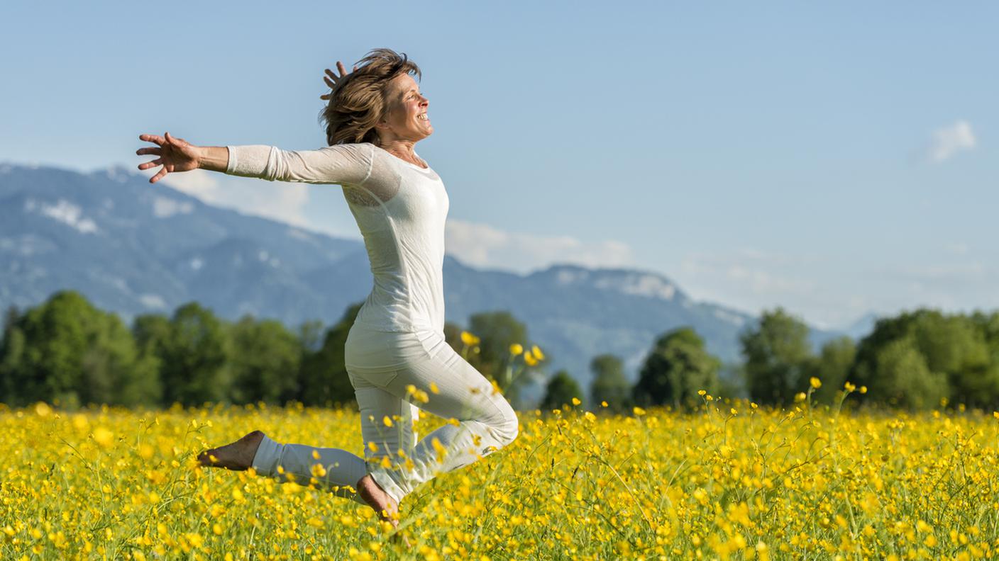 Donna matura felice saltando fiori di Prato, Salute e benessere estate