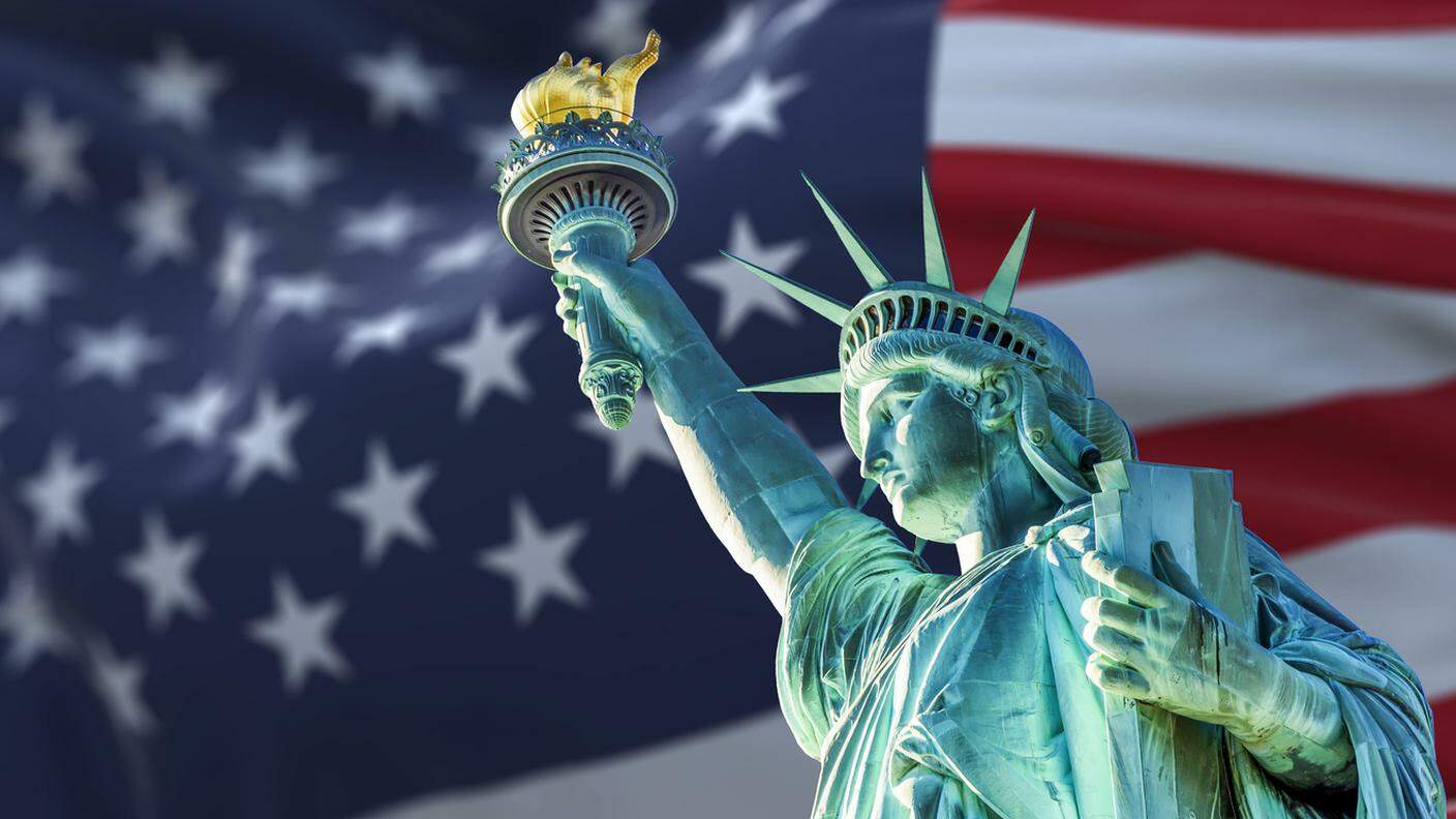 USA Statua della libertà con la bandiera sfocata americana sventolando sullo sfondo