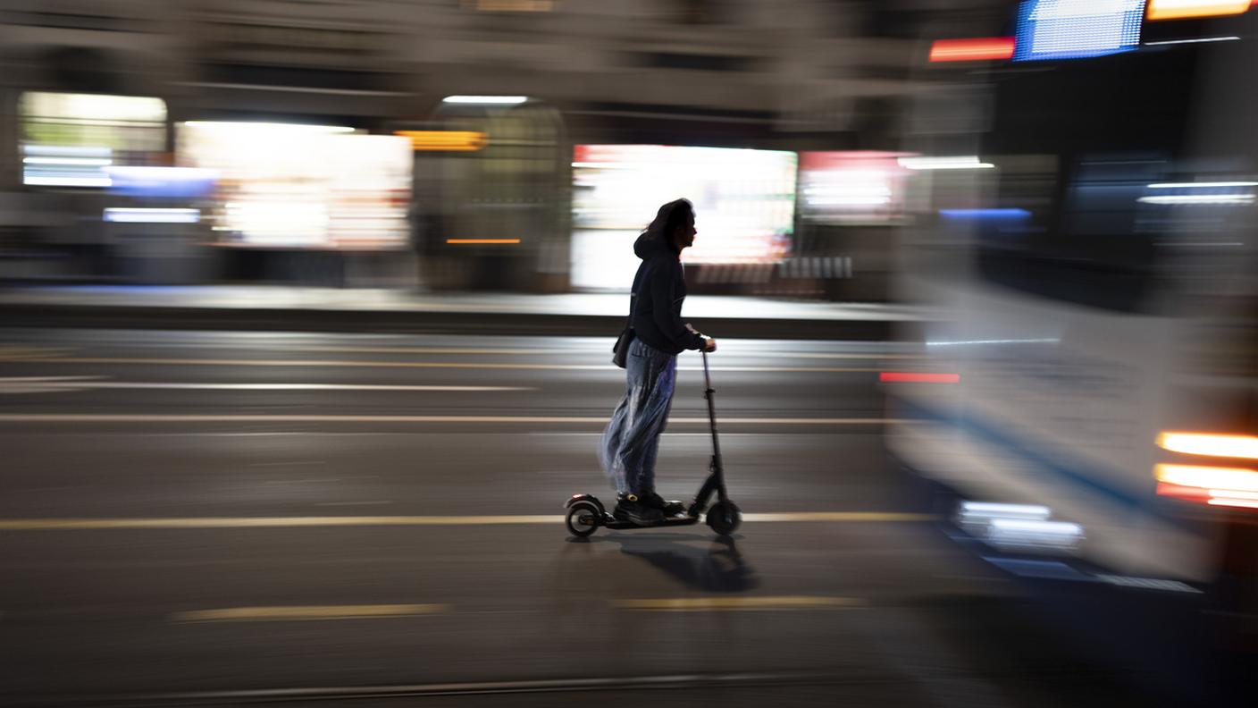 Una persona guida un monopattino elettrico di notte in una strada della città di Ginevra e supera un autobus urbano fermo, fotografata venerdì 5 giugno 2026 a Ginevra.