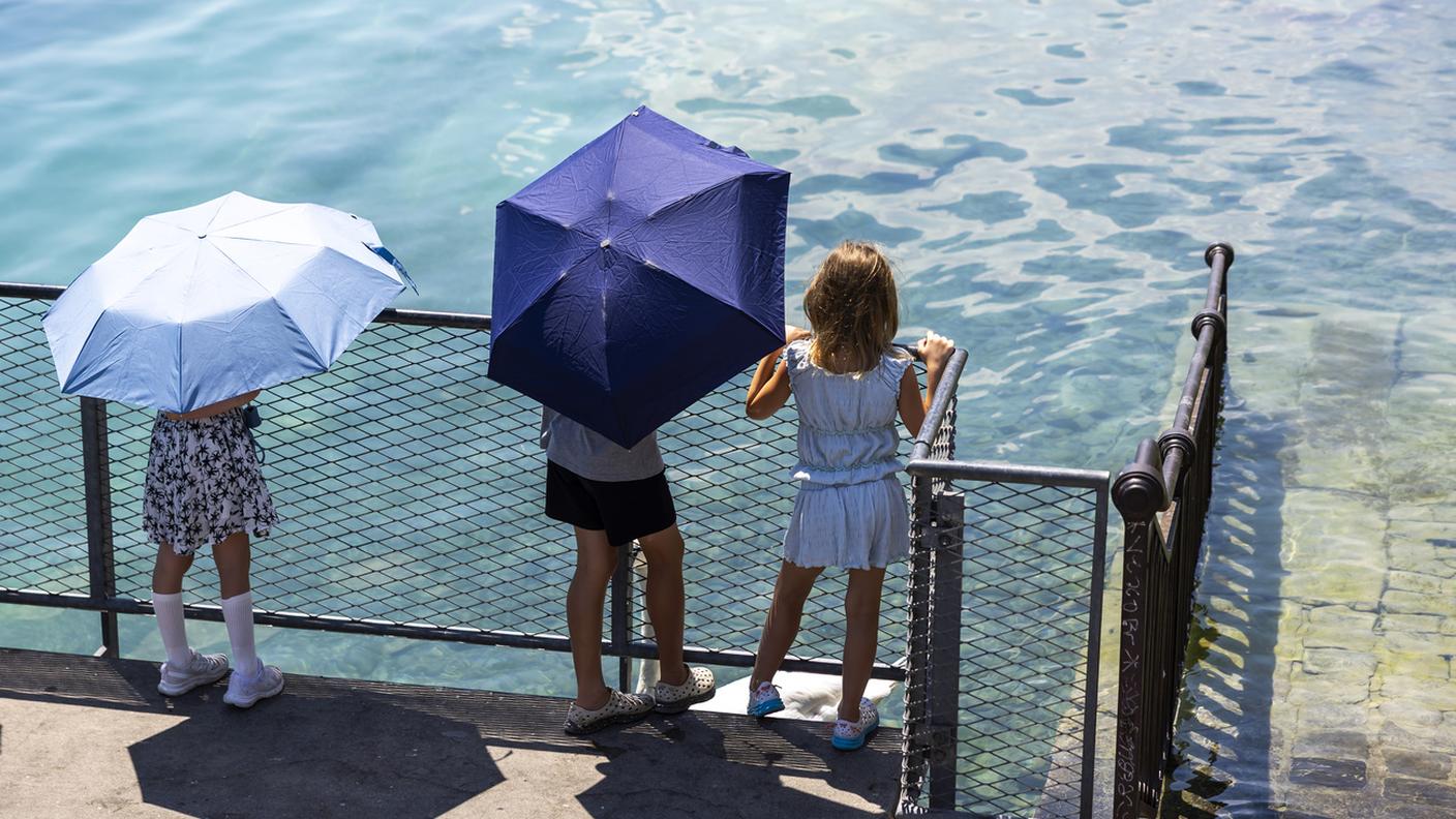 Dei bambini si proteggono dal sole con degli ombrelli mentre osservano un cigno sulle rive del lago Lemano, durante i giorni di attivazione del piano canicola da parte del Cantone di Ginevra, lunedì 30 giugno 2025 a Ginevra.