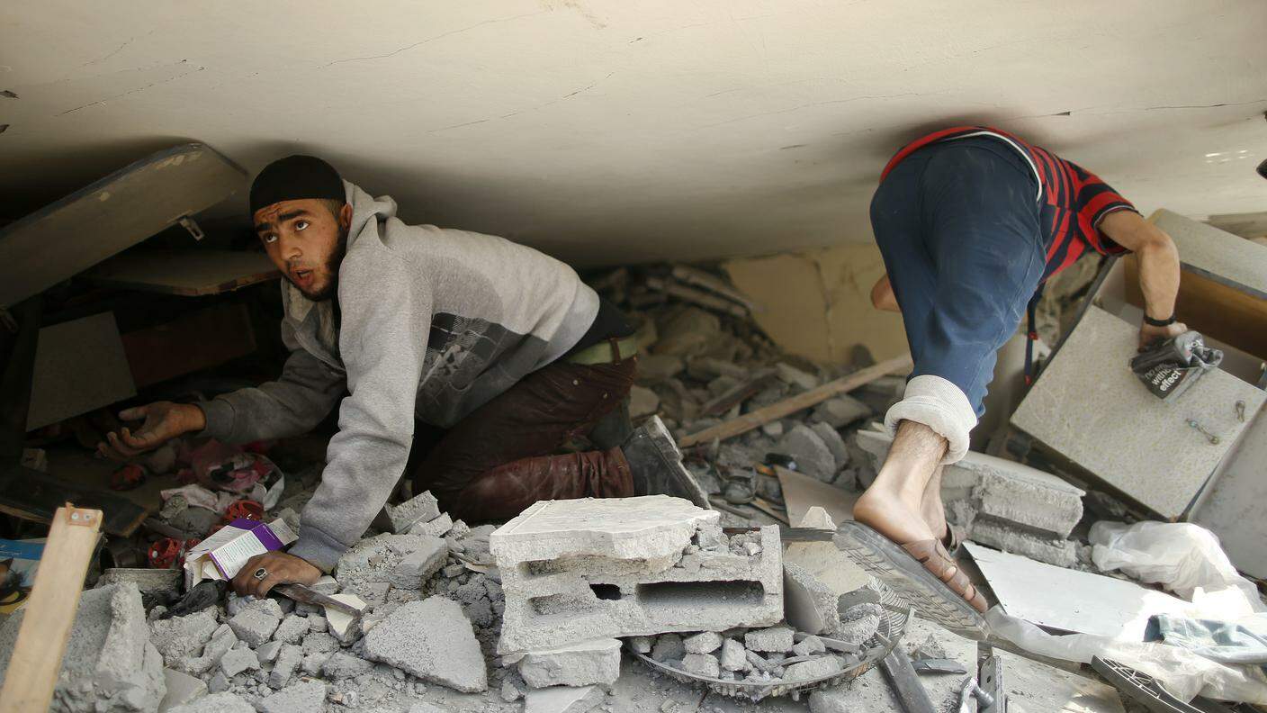 Due ragazzi palestinesi cercano i loro averi in quel che è rimasta della loro casa