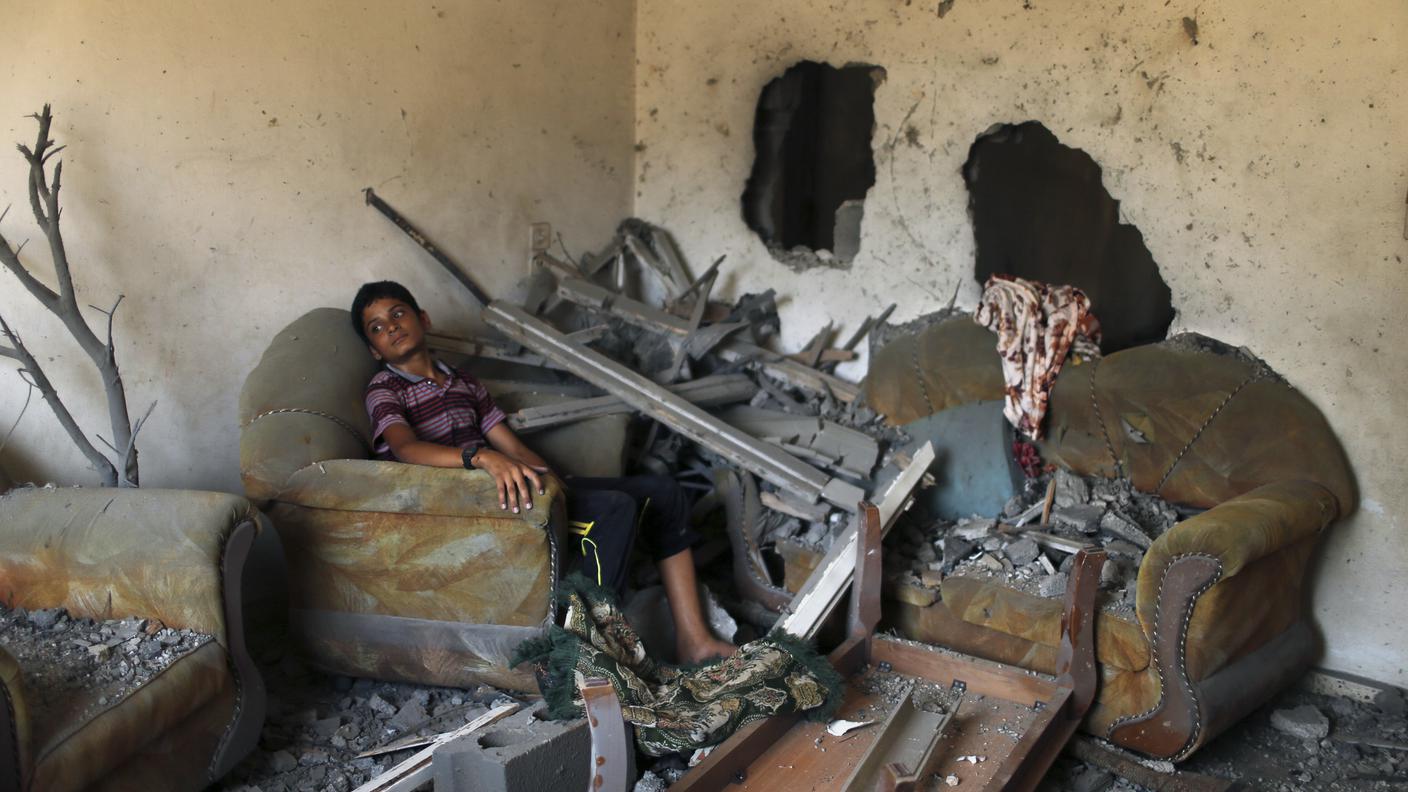 Un ragazzo palestinese siede fra le macerie della sua casa