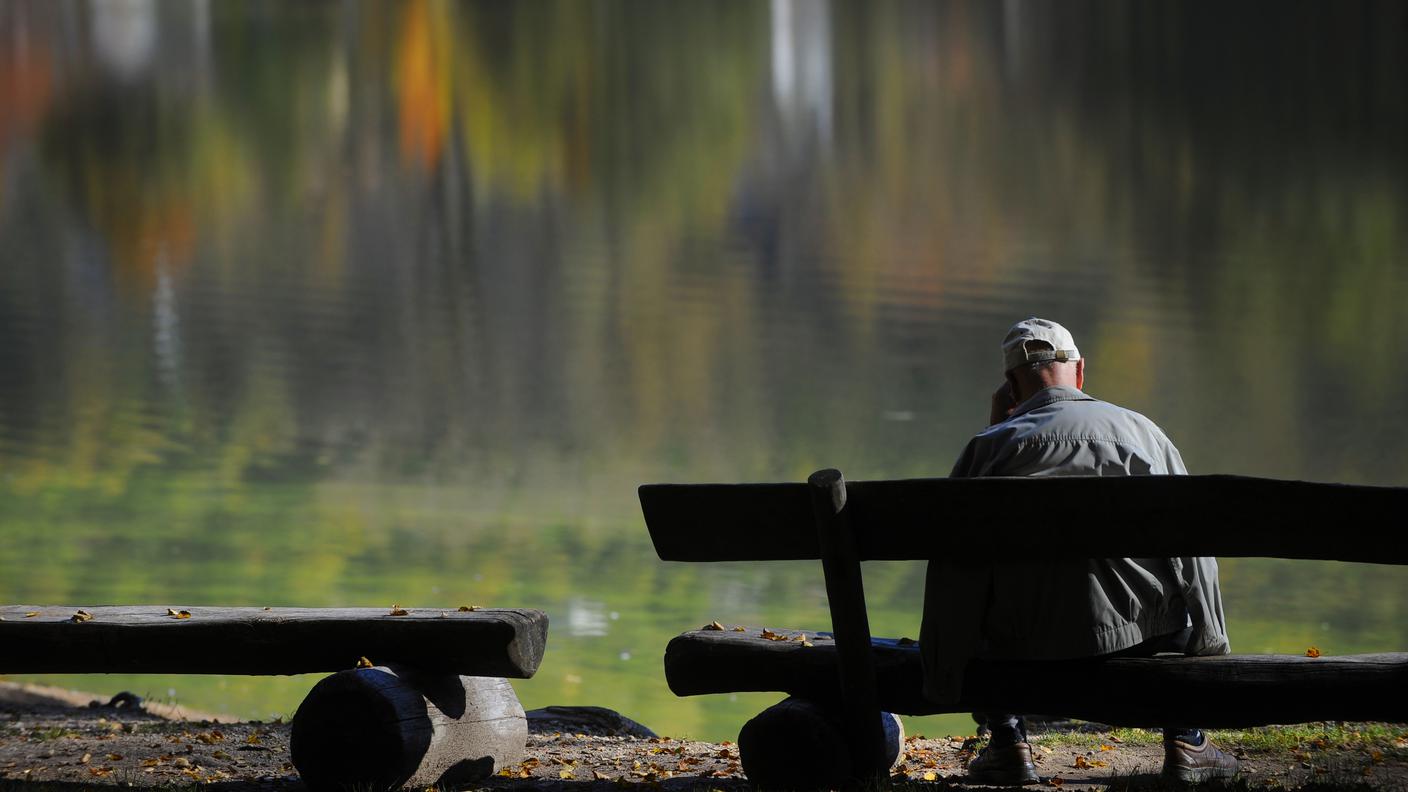Un anziano su una panchina osserva il lago con i colori autunnali