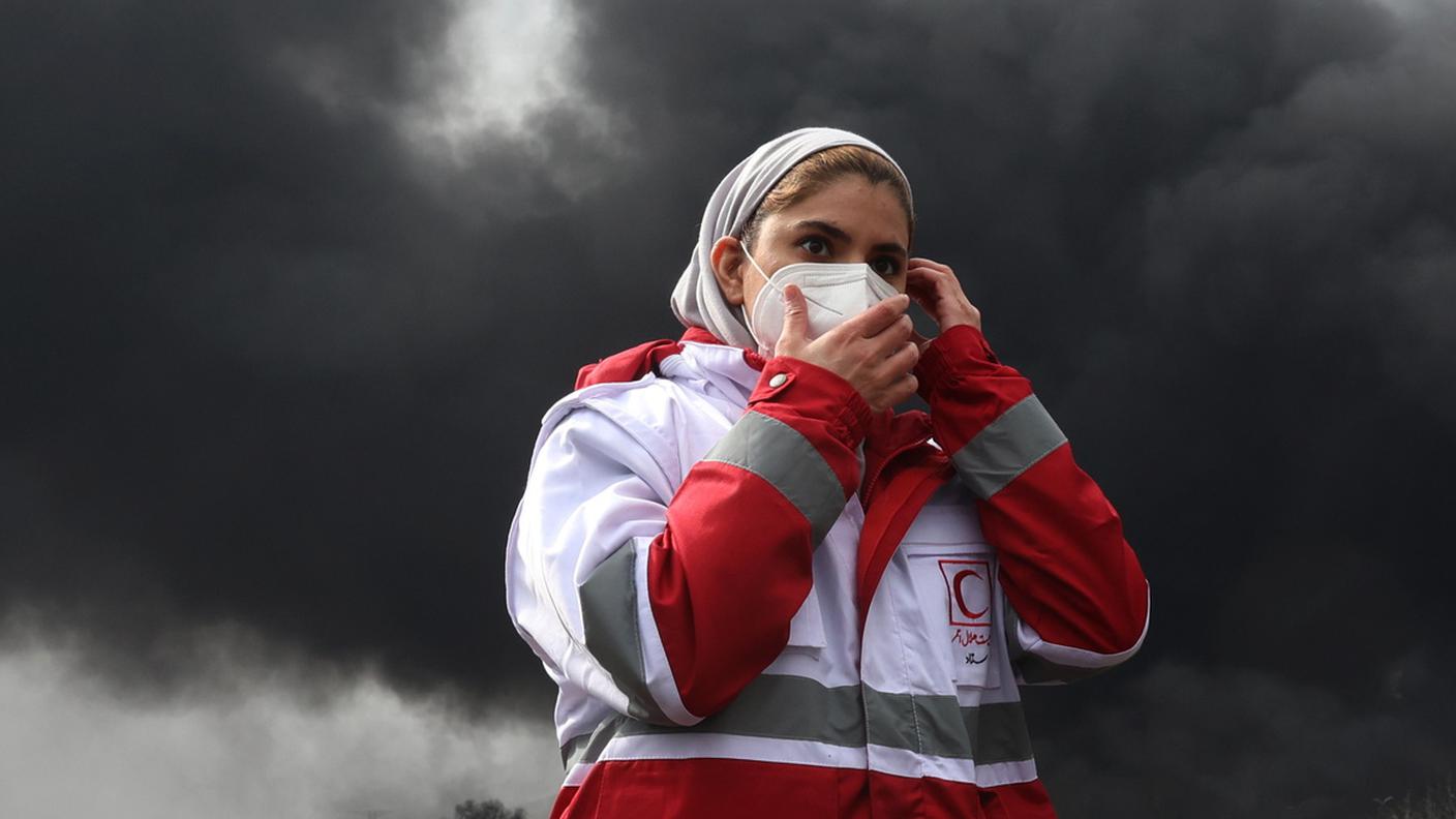 Iran, 8 marzo 2026: un membro della Mezzaluna Rossa iraniana cammina nel fumo proteggendosi con una mascherina 