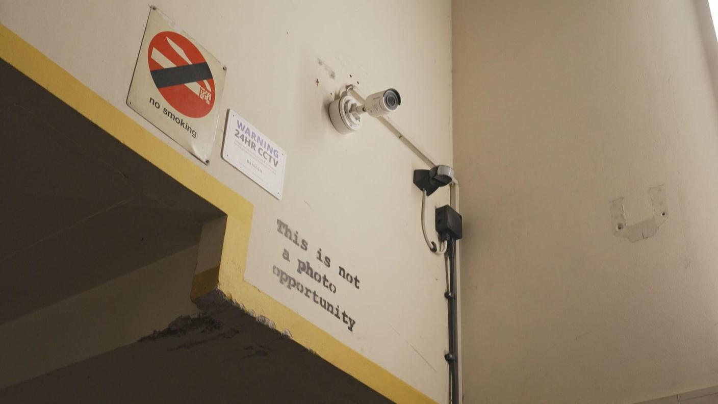 Un'iscrizione di Banksy "This is not a photo opportunity" sotto una telecamera di sorveglianza del garage