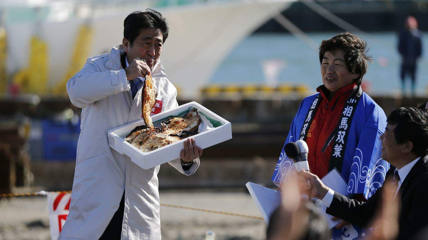 Il premier Shinzo Abe assapora davanti ai presenti un pesce pescato al largo di Fukushima, dicembre 2014