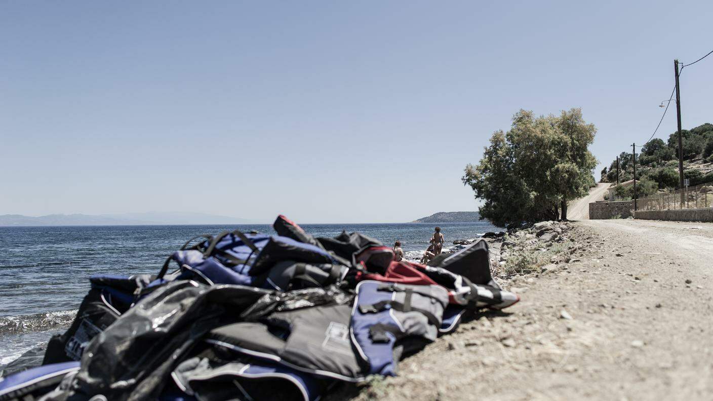 Alcuni turisti fanno il bagno nel mare sull'isola di Lesbo, in Grecia. In primo piano, una presenza alla quale sembrano essersi abituati: giubbotti di salvataggio indossati dai migranti e abbandonati al momento dello sbarco.