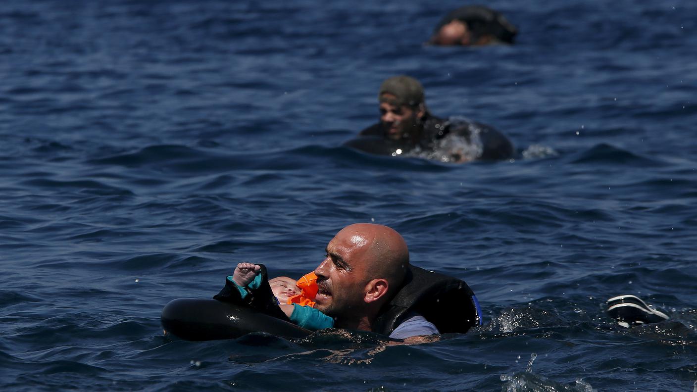 Un profugo siriano porta suo figlio in braccio mentre nuota al largo dell’isola di Lesbo, in Grecia, dopo che il gommone su cui viaggiavano è naufragato. 