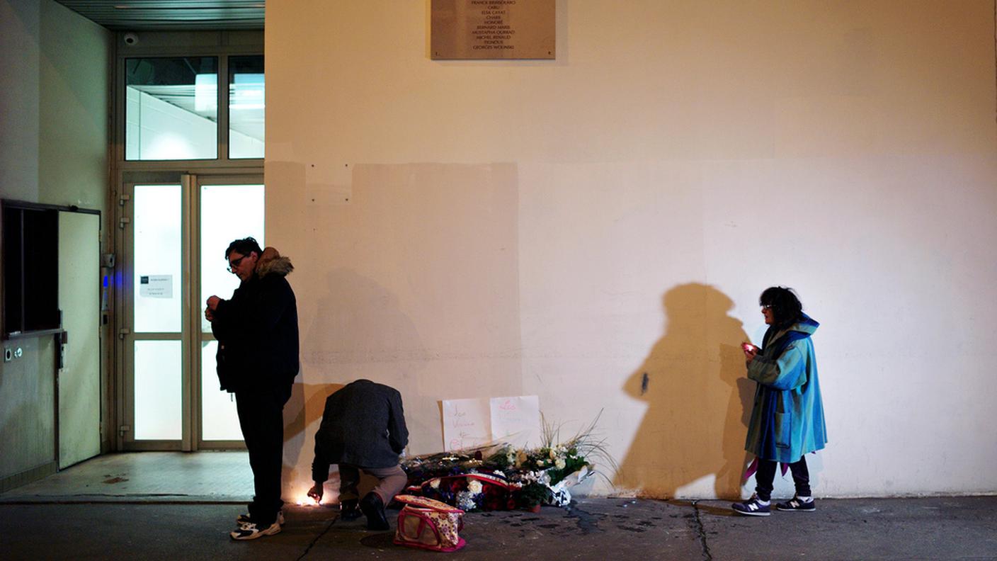 Alcune persone accendono candele sotto la targa con i nomi degli uccisi, davanti al palazzo dove aveva sede la redazione