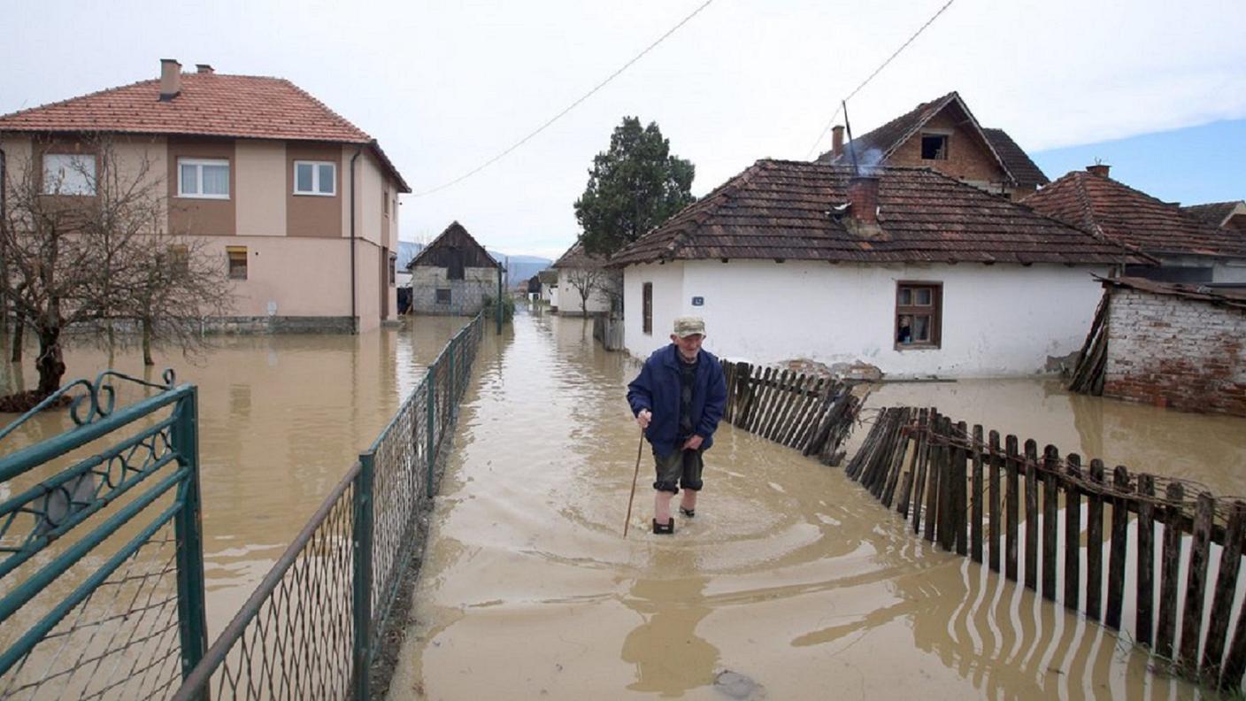 Un anziano attraversa una strada inondata presso Pozega, in Serbia