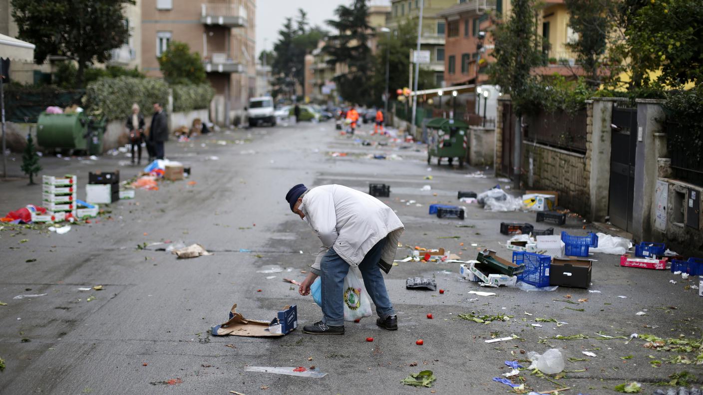 Un uomo raccoglie scarti di cibo, abbandonati alla chiusura di un mercato di strada