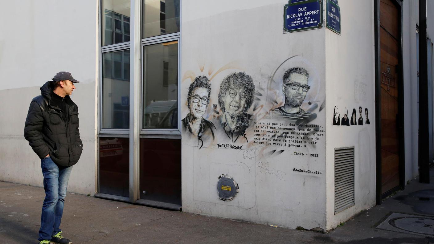 Un uomo davanti alla sede di Charlie Hebdo dove spiccano i ritratti dei giornalisti uccisi