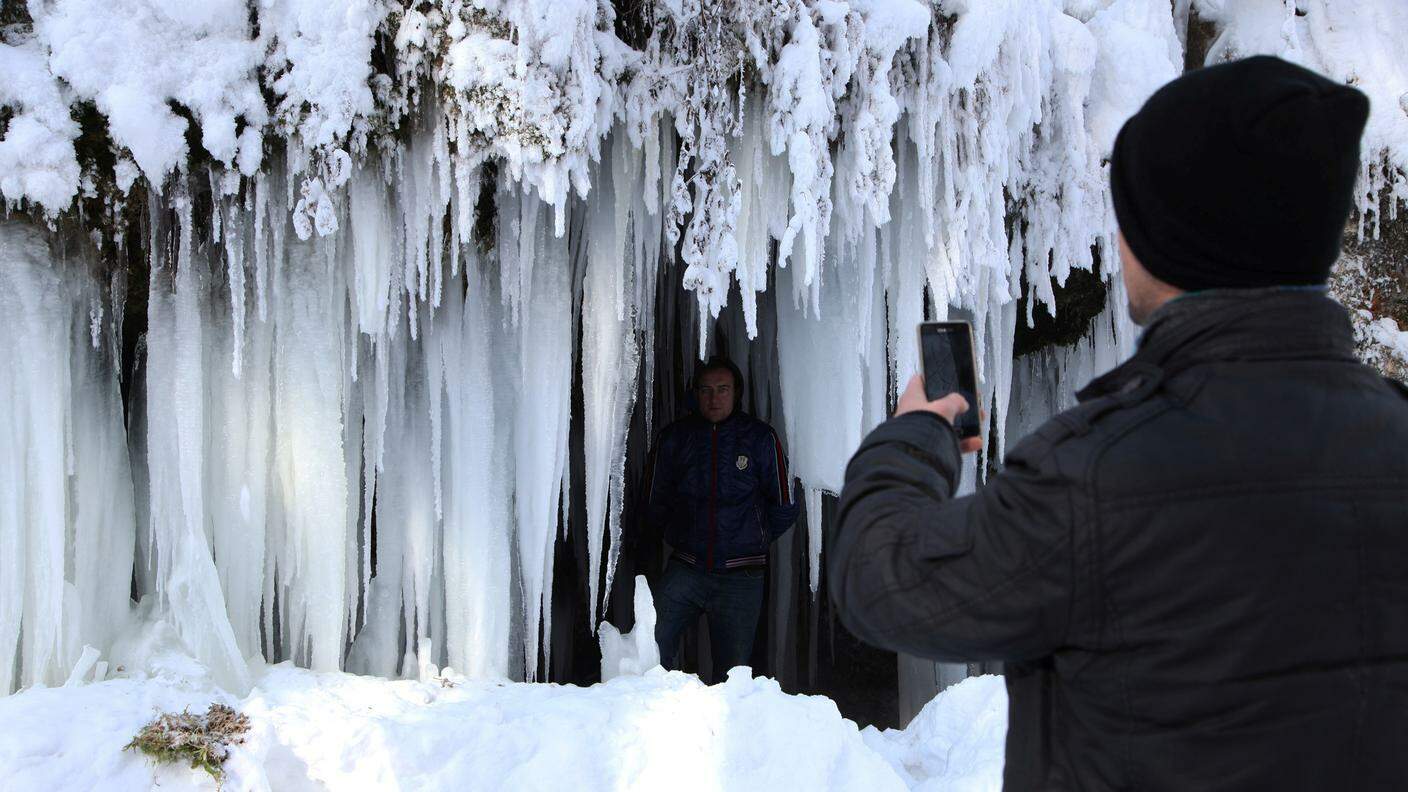Un ragazzo scatta una foto a un amico sotto una cascata gelata a Jezerc, in Kosovo