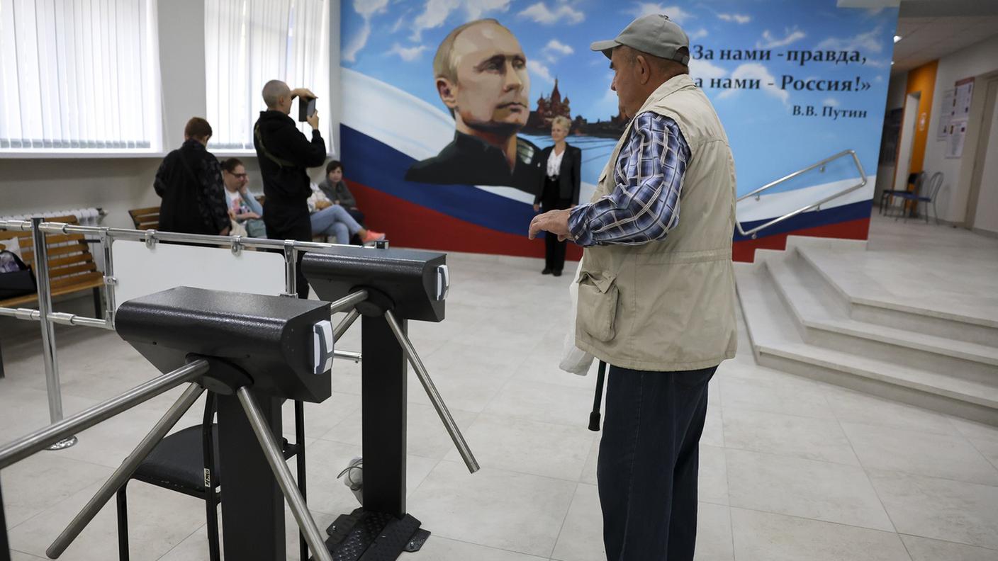 Un elettore lascia il seggio a Donetsk, sotto l'occhio vigile di Putin