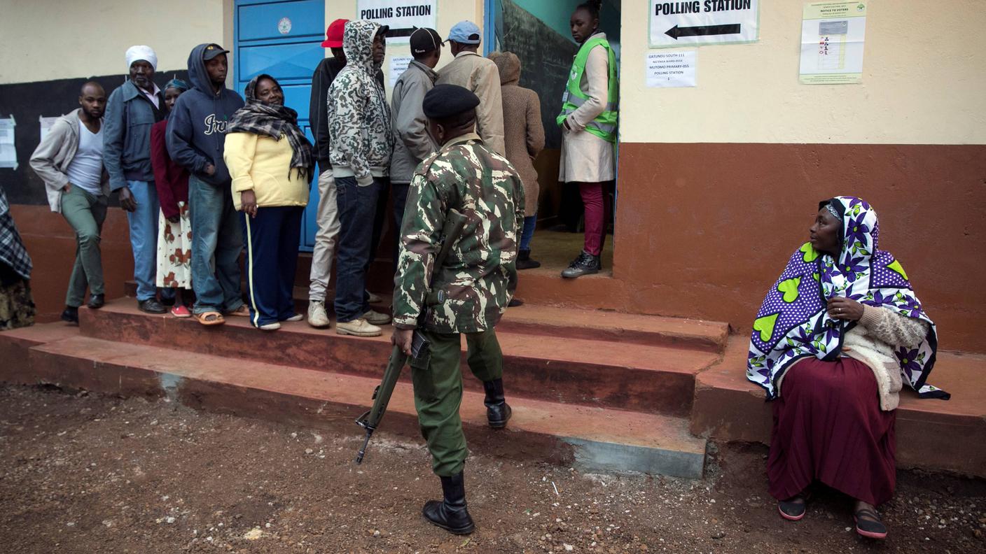Cittadini keniani in fila per votare sotto l'occhio vigile di un militare