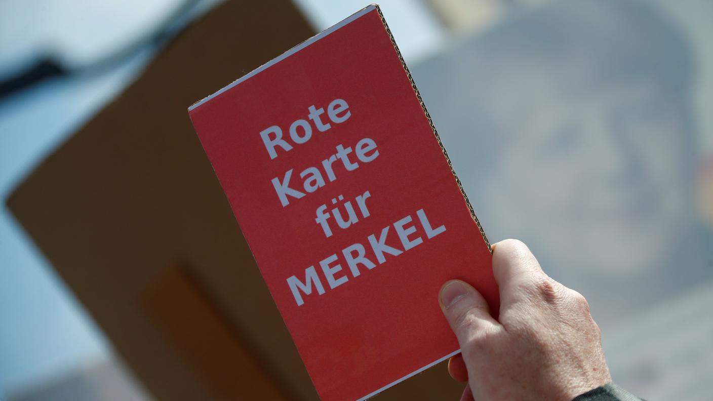 Un manifestante ostile alla cancelliera tedesca mostra un cartellino rosso per la Merkel