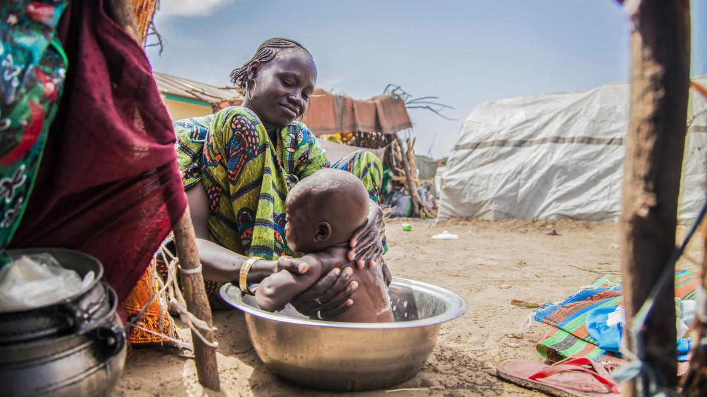 Una mamma lava il suo bimbo in un campo profughi in Nigeria