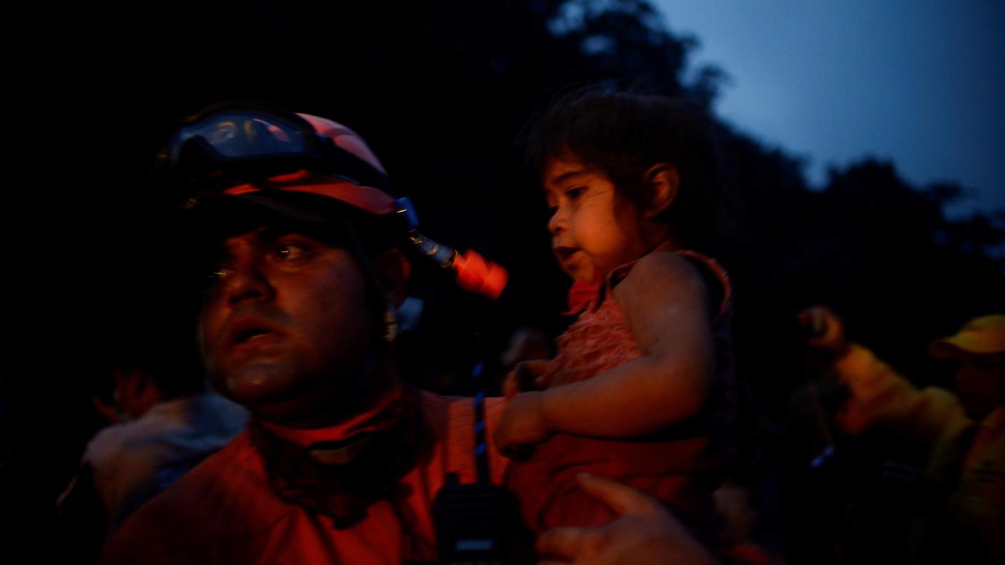 Un soccorritore porta in salvo un bambino alla luce dell'eruzione del vulcano