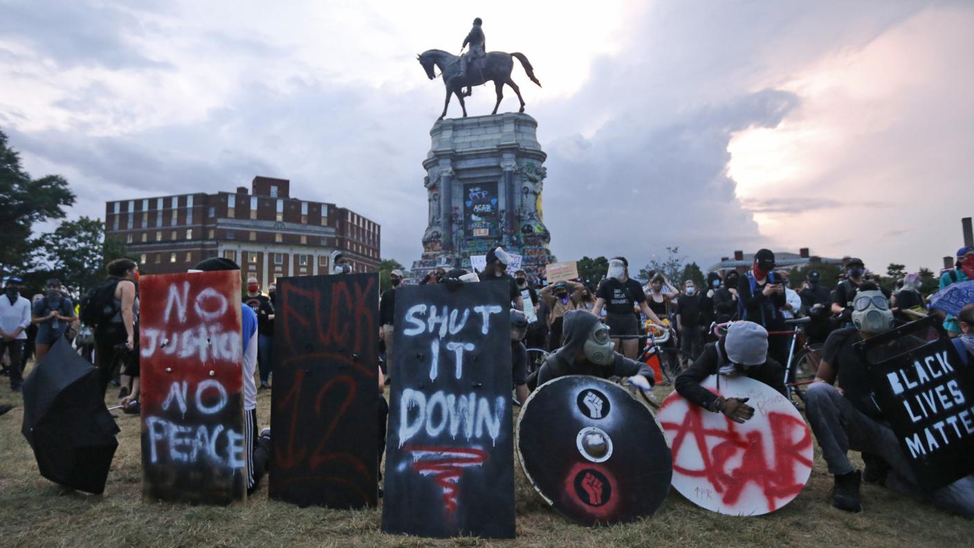 Dimostranti e cartelli di protesta attorno alla statua