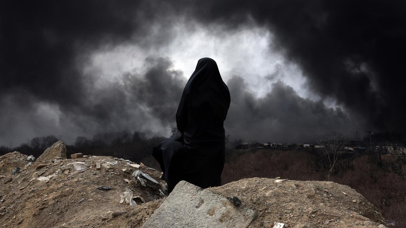  Una donna osserva il fumo nero che si leva da un deposito di petrolio a Shahran, nella periferia nord di Teheran