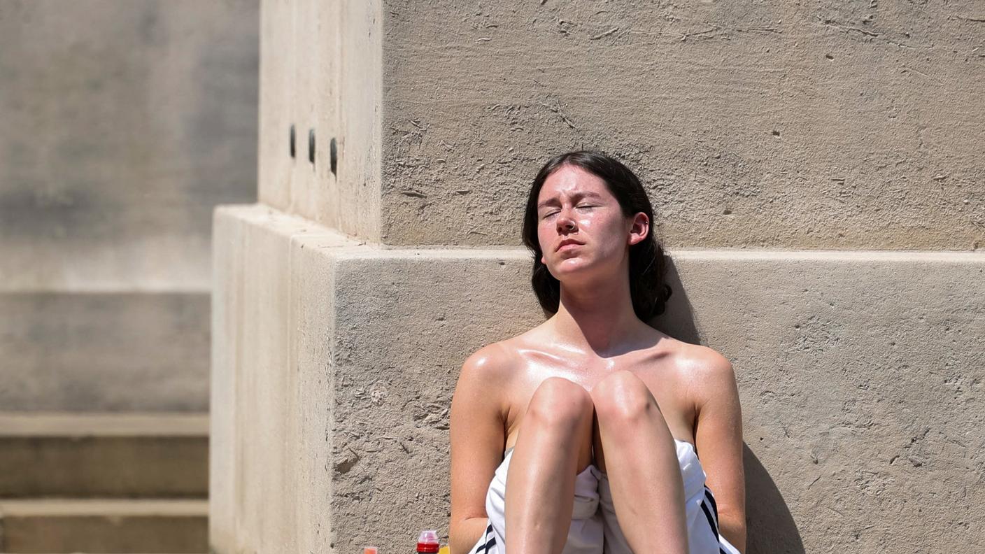 Una donna si riposa appoggiata a un muro a Manchester, nel mezzo di un'ondata di calore, mentre la Gran Bretagna registra temperature record che bloccano le scuole e le reti di trasporto