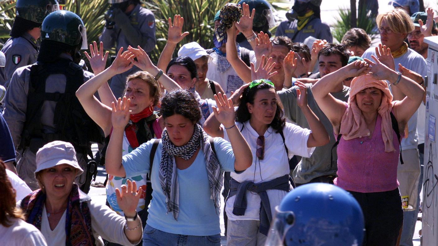 Manifestanti no global alzano le mani mentre vengono condotti via da agenti della polizia antisommossa nel centro di Genova