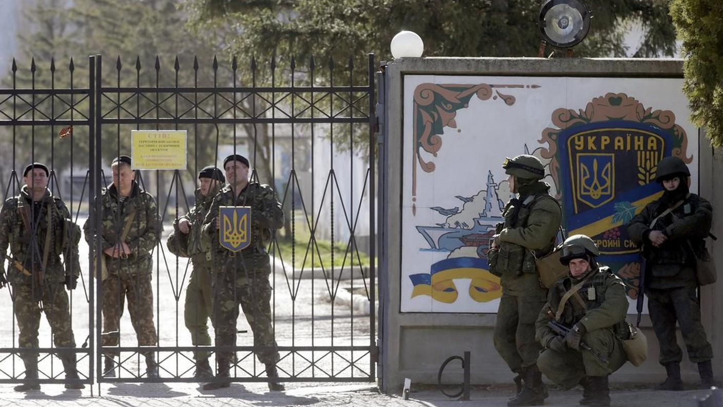 Soldati ucraini dietro al cancello  e uomini armati filo russi  in una caserma di Perevalnoye, in Crimea