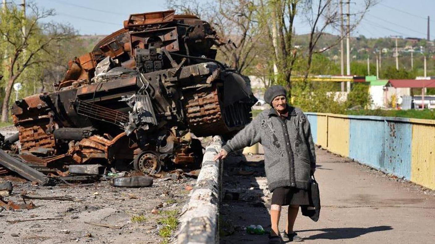 Una anziana signora ucraina vicino a un mezzo blindato distrutto