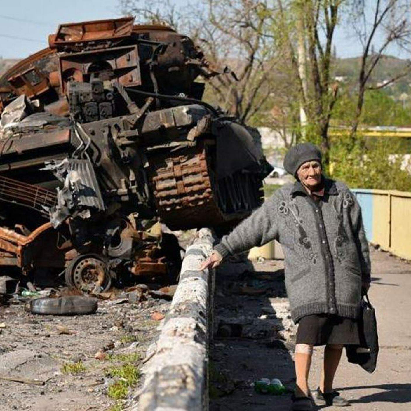 Una anziana signora ucraina vicino a un mezzo blindato distrutto