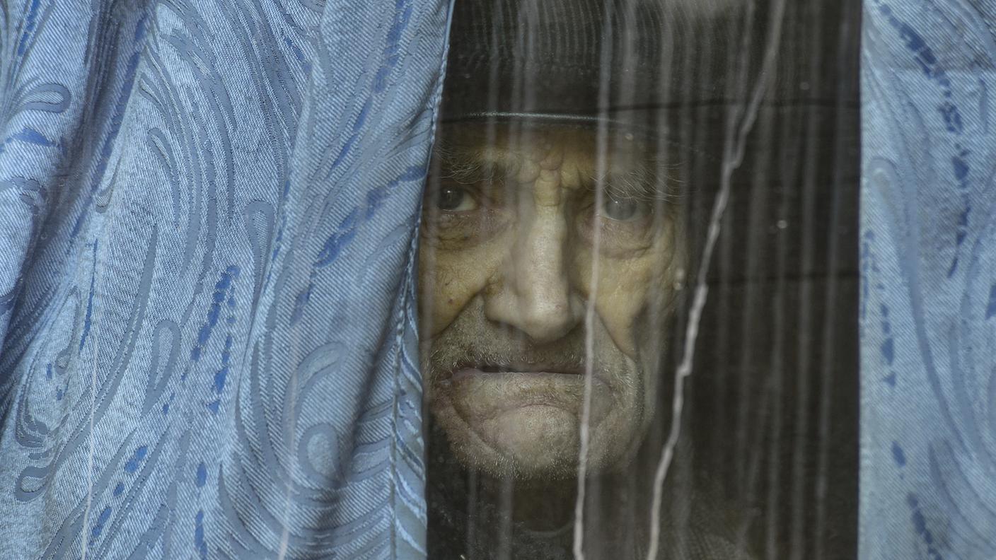 Un anziano abitante di Kherson guarda dalla finestra della sua casa nella città martoriata