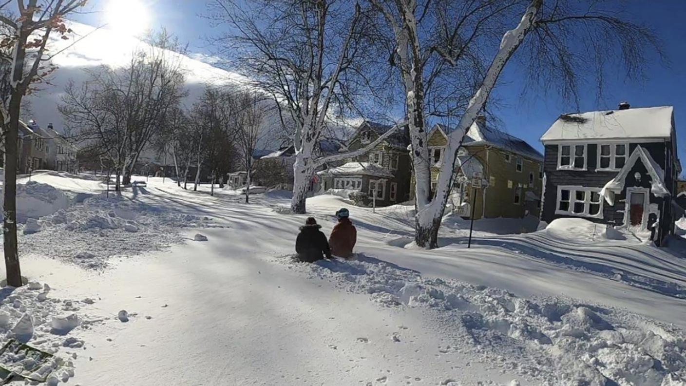 Due persone camminano in mezzo alla neve su una strada di Buffalo domenica
