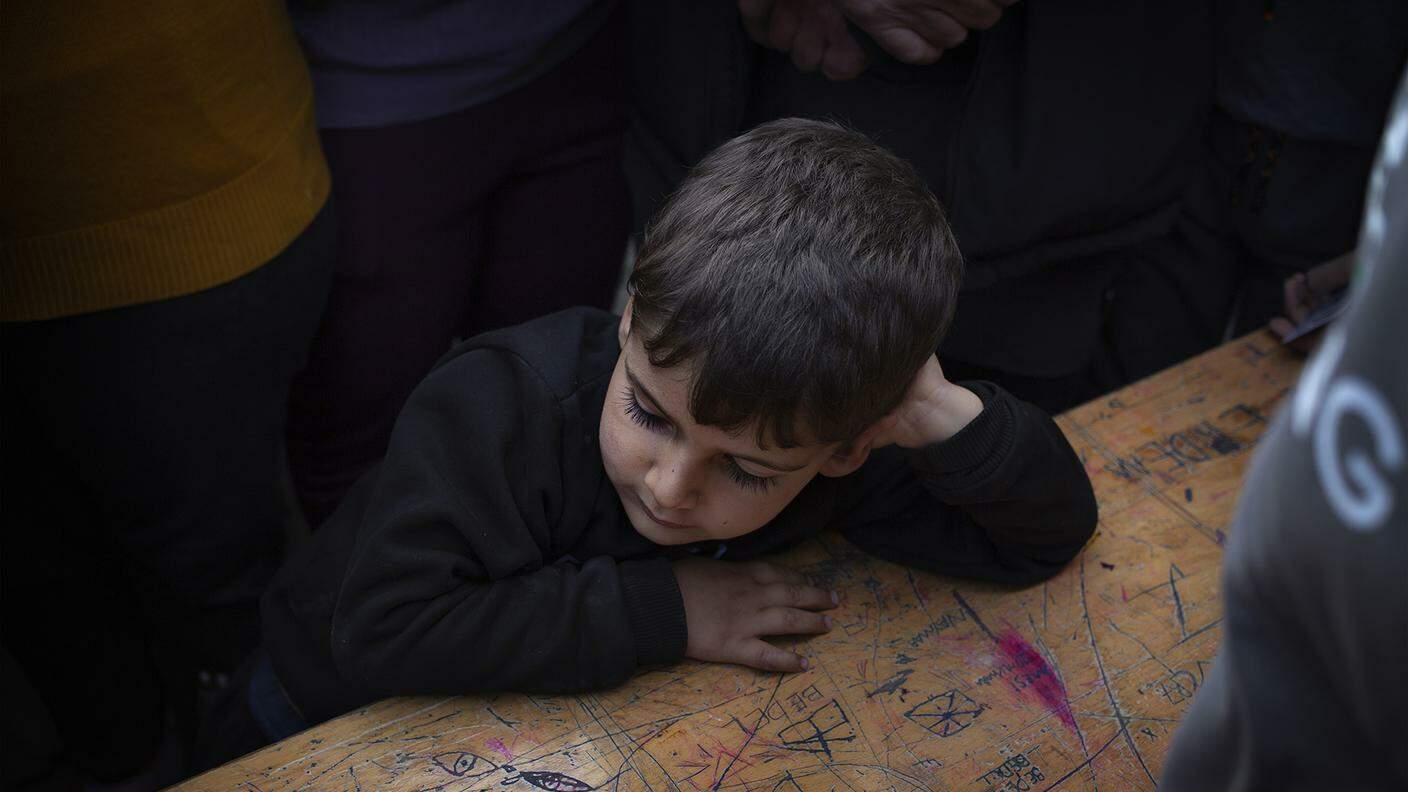 Un bambino attende annoiato in attesa che i suoi parenti abbiano raccolto gli aiutialimentari di un'associazione umanitaria