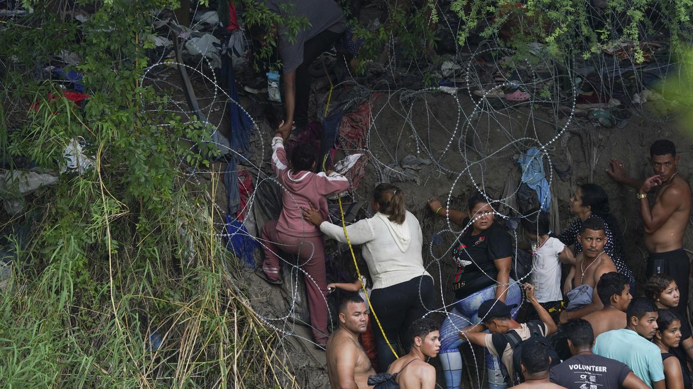 Migranti attraversano una barriera di filo spinato per entrare negli Stati Uniti dopo aver attraversato il Rio Bravo 