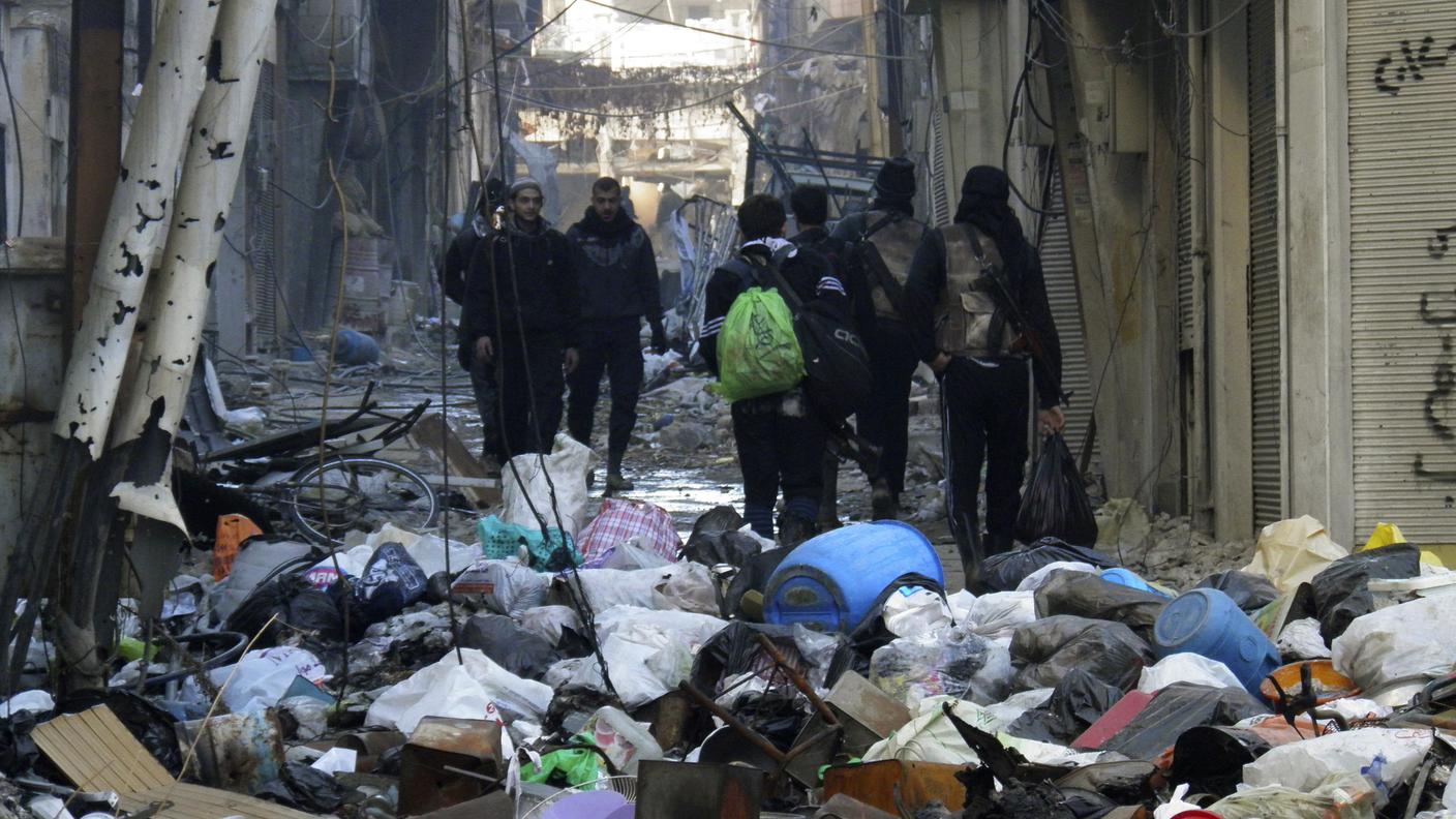 Civili e militari siriani camminano lungo una strada distrutta e piena di rifiuti a Homs, città assediata dalle forze lealiste da un anno e mezzo