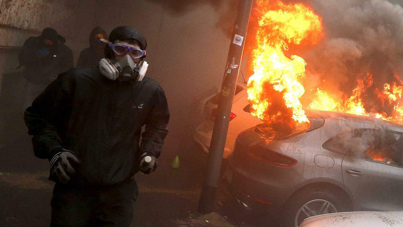 Un manifestante a fianco di un SUV Porsche dato alle fiamme
