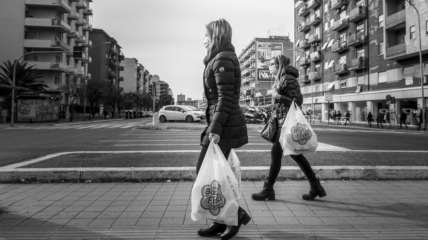 Due donne di ritorno dalla spesa, a distanza di oltre un metro l'una dall'altra, con guanti e mascherina