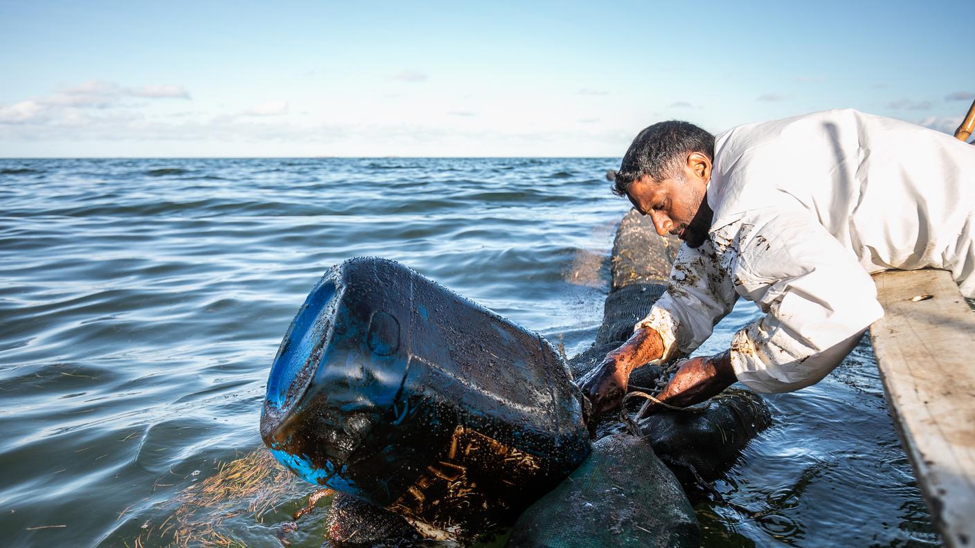 Uno dei pescatori colloca in mare le boe artigianali per contenere l'avanzata del greggio