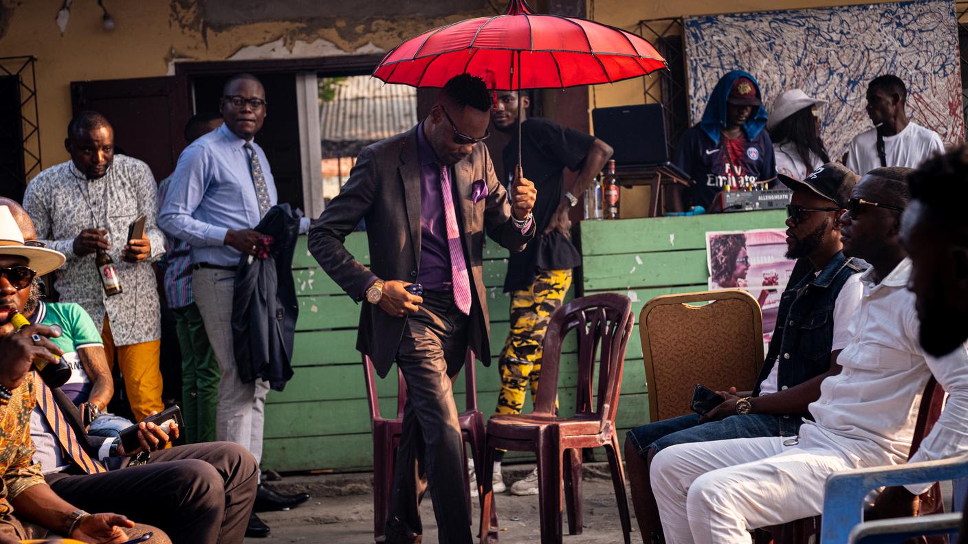 Un sapeur si mette in posa durante una sfilata in un combat d’esthètes (lotta tra esteti) in un locale del quartiere Bacongo a Brazzaville. Ad osservarlo e giudicarlo ci sono decine di altri sapeurs e sapeuses assieme ai ngembos, gli ammiratori della Sape.