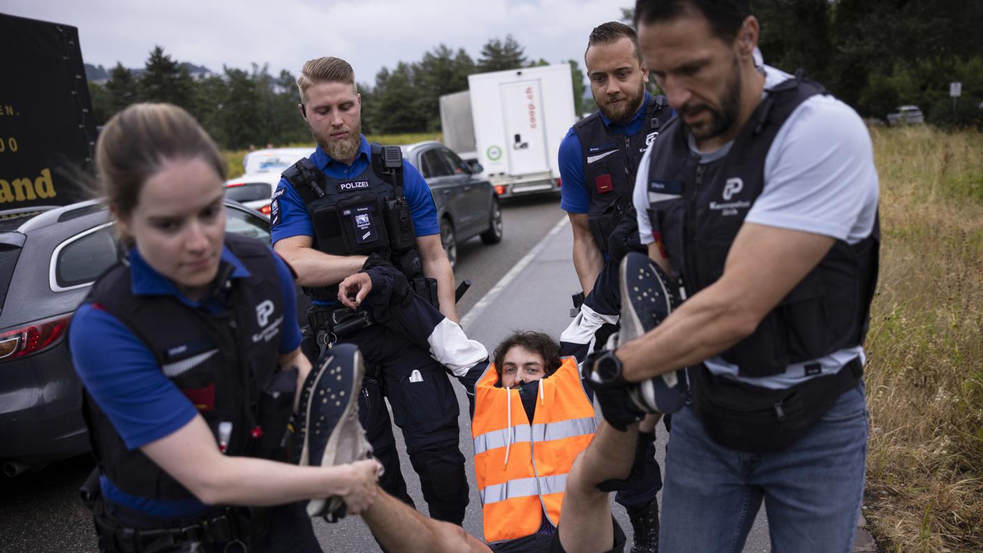 Agenti della polizia zurighese portano via di peso un manifestante che bloccava l'autostrada