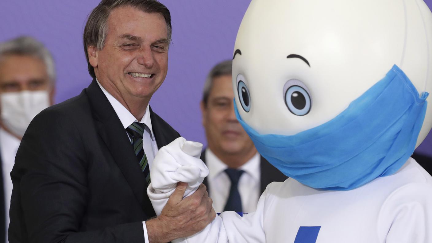 Il presidente brasiliano Bolsonaro con la "mascotte" della campagna di vaccinazione