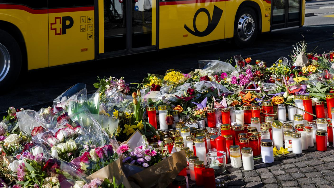 Un autopostale transita davanti al luogo del dramma, dove ora sono state posate candele e fiori