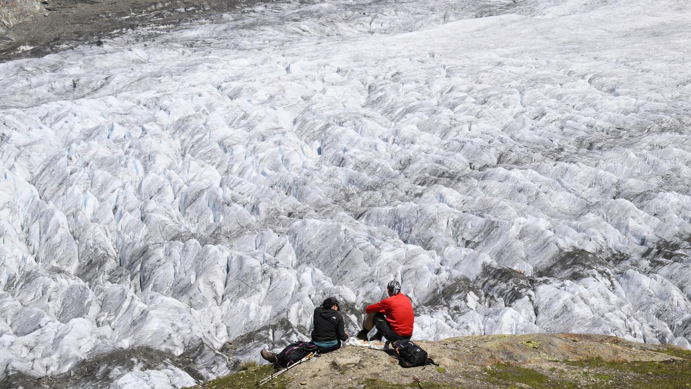 Due persone mangiano e ammirano il panorama del ghiacciaio dell'Aletsch, il più lungo d'Europa, nei pressi di Bettmeralp, in Svizzera, venerdì 15 luglio 2022. Il ghiacciaio dell'Aletsch si estende per oltre 23 chilometri, dalla sua area di formazione nella regione della Jungfrau, a circa 4'000 metri di quota, fino alla gola della Massa, in Vallese, quasi 2'500 metri più in basso.