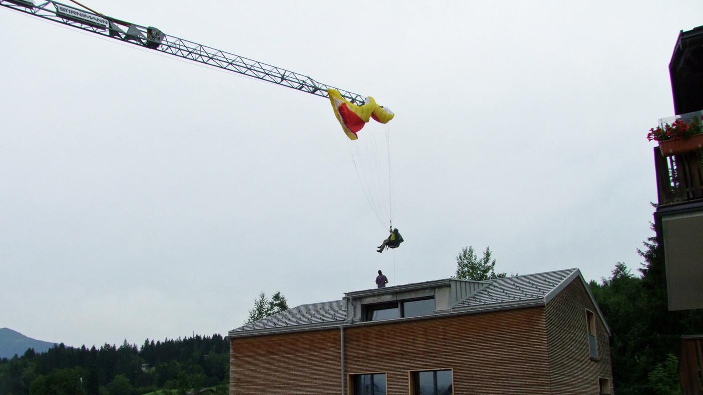 Il parapendista appeso al braccio della gru